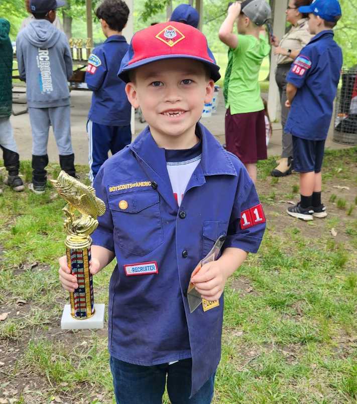 Cub Scout wearing uniform smiling and holding a trophy in the outdoors